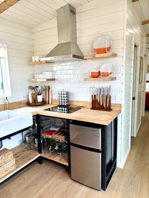 kitchen with light wood-style flooring, freestanding refrigerator, wall chimney range hood, and open shelves