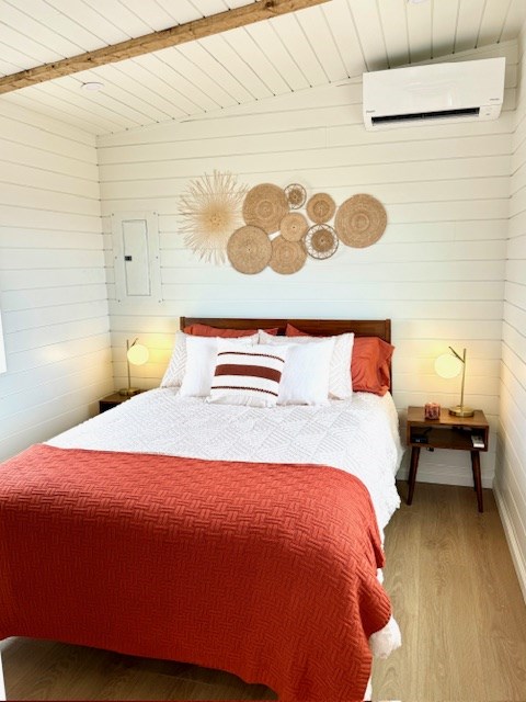 bedroom with an AC wall unit, wooden ceiling, beam ceiling, and wood finished floors