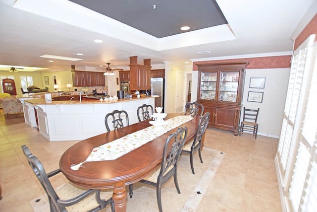 dining room with ceiling fan, a raised ceiling, ornamental molding, and sink