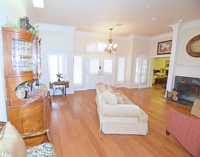 living room with a high end fireplace, french doors, light wood-type flooring, ornamental molding, and a notable chandelier