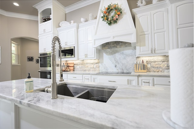 kitchen with backsplash, premium range hood, white cabinets, light stone countertops, and appliances with stainless steel finishes