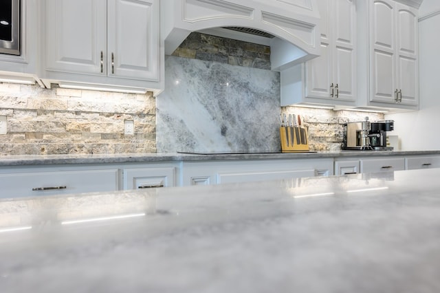 kitchen featuring decorative backsplash, light stone countertops, black electric stovetop, premium range hood, and white cabinets