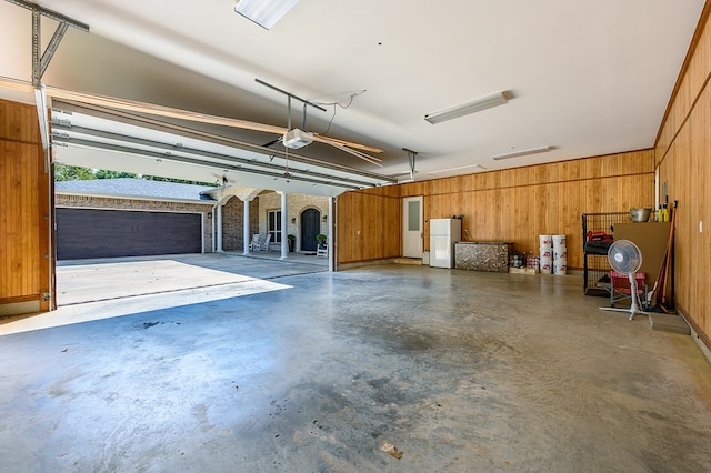 garage with white fridge, a garage door opener, and wood walls