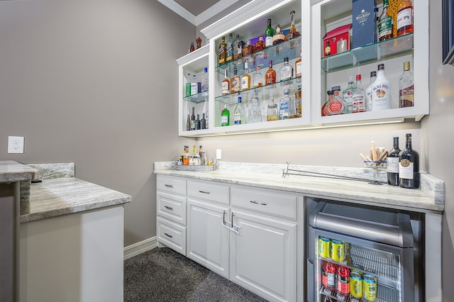 bar featuring wine cooler, light stone counters, crown molding, dark colored carpet, and white cabinetry