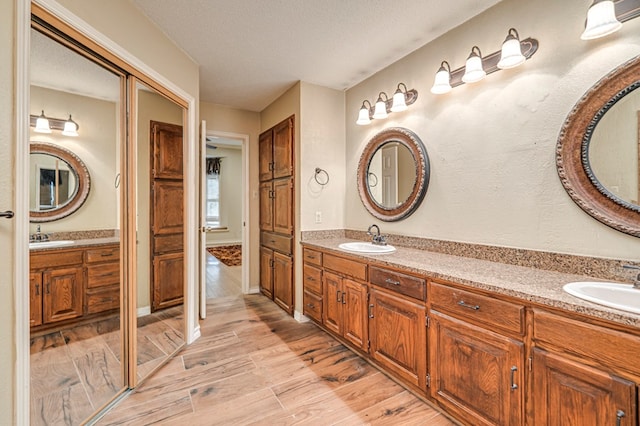 bathroom with double vanity, a textured ceiling, wood finished floors, and a sink