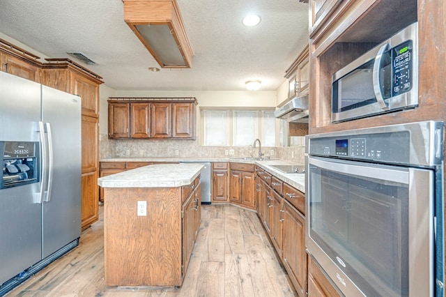 kitchen with light countertops, brown cabinetry, appliances with stainless steel finishes, and a center island