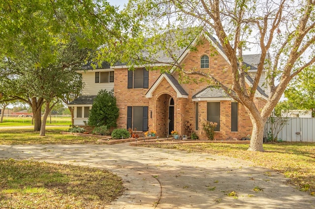 traditional-style house featuring brick siding, roof with shingles, a front lawn, and fence