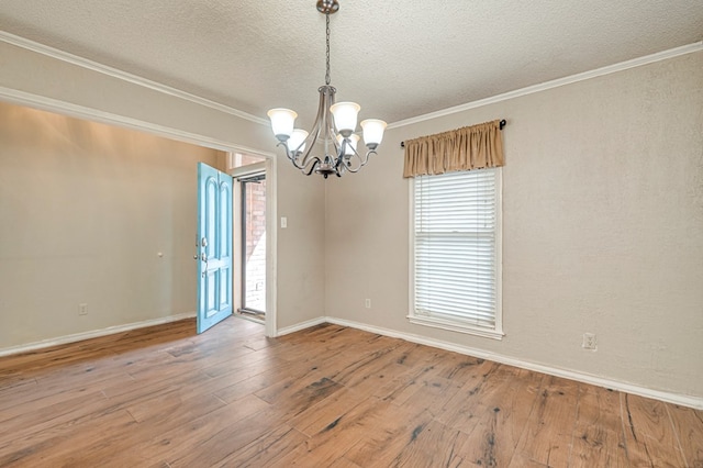 empty room featuring ornamental molding, a textured ceiling, wood-type flooring, an inviting chandelier, and baseboards