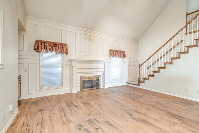 unfurnished living room featuring stairway, a decorative wall, wood finished floors, and a tile fireplace