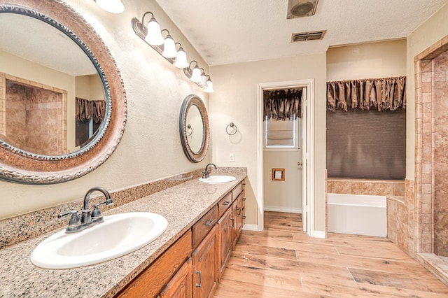 bathroom with visible vents, a textured ceiling, wood finished floors, and a sink