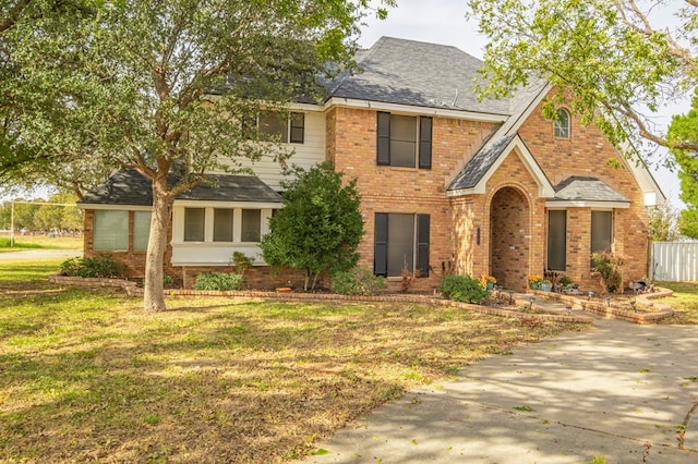 view of front of home with a front yard, brick siding, and a shingled roof