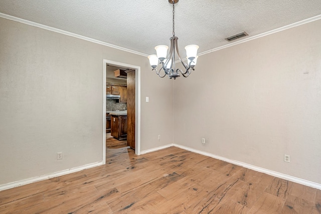 spare room featuring a notable chandelier, visible vents, wood-type flooring, and ornamental molding