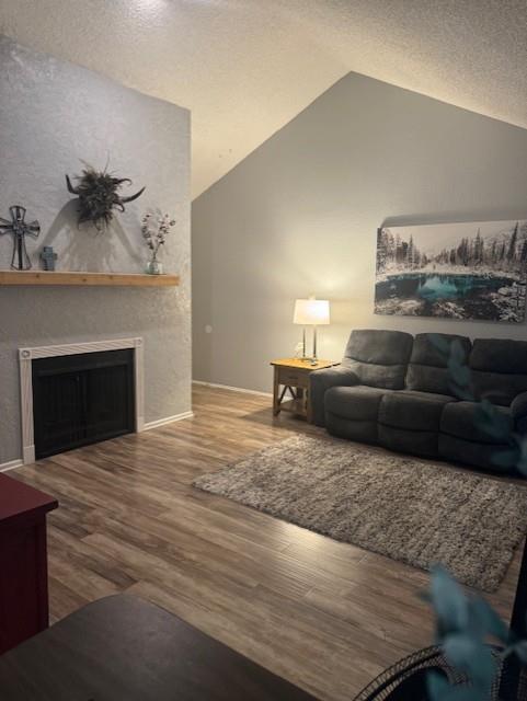 living room featuring wood-type flooring, a textured ceiling, and vaulted ceiling