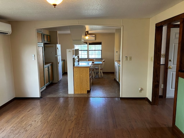 kitchen featuring dark wood-type flooring, white refrigerator, an AC wall unit, ceiling fan, and a textured ceiling