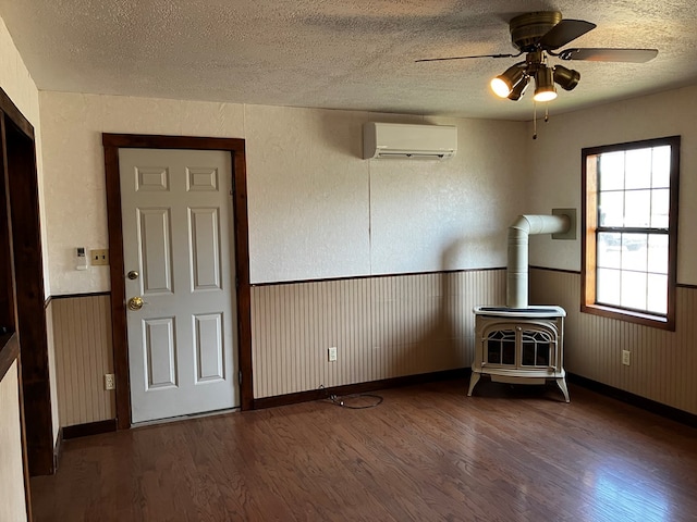 empty room with a wall mounted air conditioner, a textured ceiling, ceiling fan, dark hardwood / wood-style floors, and a wood stove