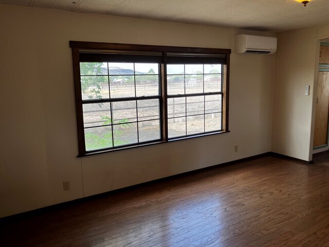 spare room featuring a wealth of natural light, dark wood-type flooring, and a wall mounted air conditioner