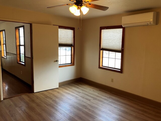 spare room featuring light hardwood / wood-style floors, a wall unit AC, and ceiling fan