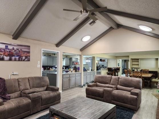 living room featuring beamed ceiling, ceiling fan, light wood-type flooring, and a textured ceiling