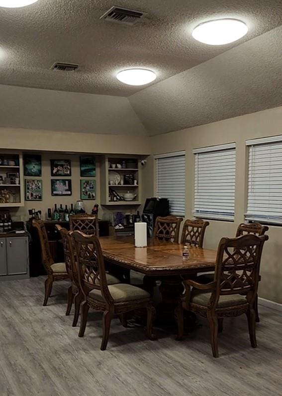 dining area with hardwood / wood-style floors, lofted ceiling, and a textured ceiling