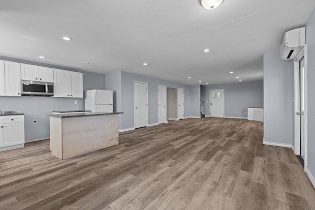 kitchen featuring stainless steel microwave, freestanding refrigerator, white cabinetry, wood finished floors, and a wall mounted air conditioner