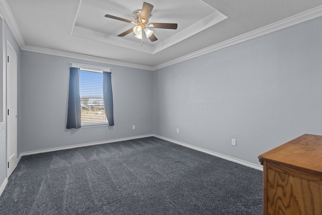 spare room with baseboards, a raised ceiling, ceiling fan, crown molding, and dark carpet