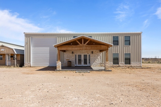 rear view of property featuring stone siding, french doors, an outdoor structure, and board and batten siding