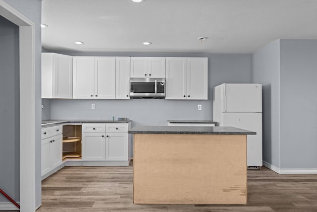 kitchen with light wood-style flooring, stainless steel microwave, white cabinets, and freestanding refrigerator