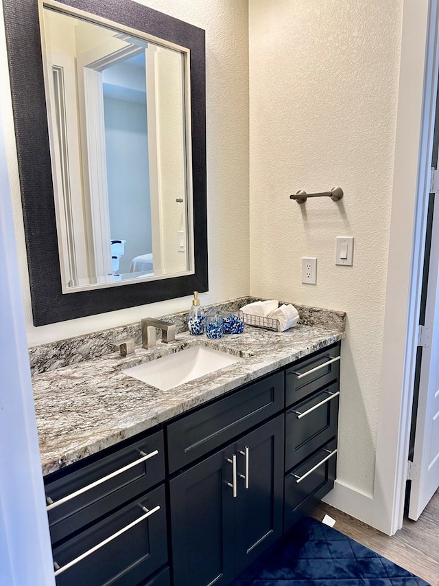 bathroom with baseboards, wood finished floors, vanity, and a textured wall