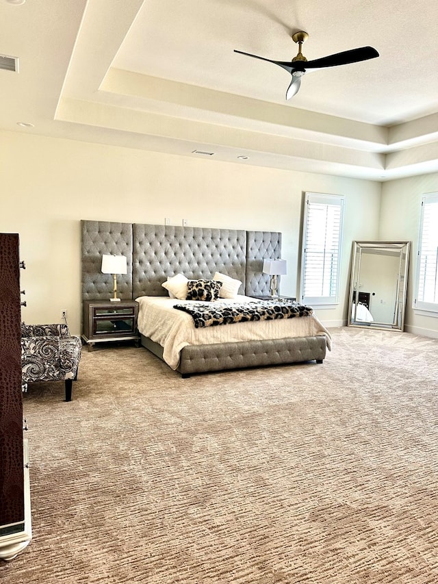 carpeted bedroom with a tray ceiling, baseboards, visible vents, and a ceiling fan