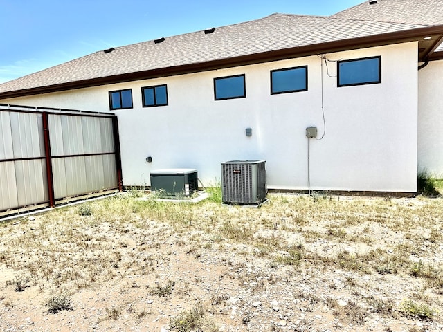 rear view of property with stucco siding, central AC, and roof with shingles