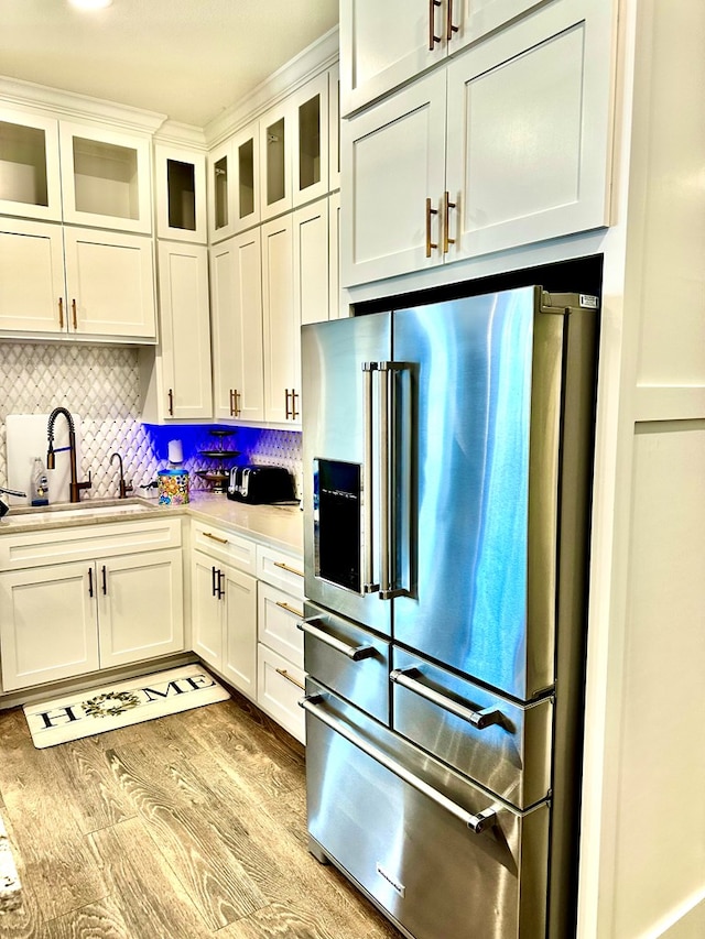 kitchen featuring light wood finished floors, light countertops, decorative backsplash, high end fridge, and a sink