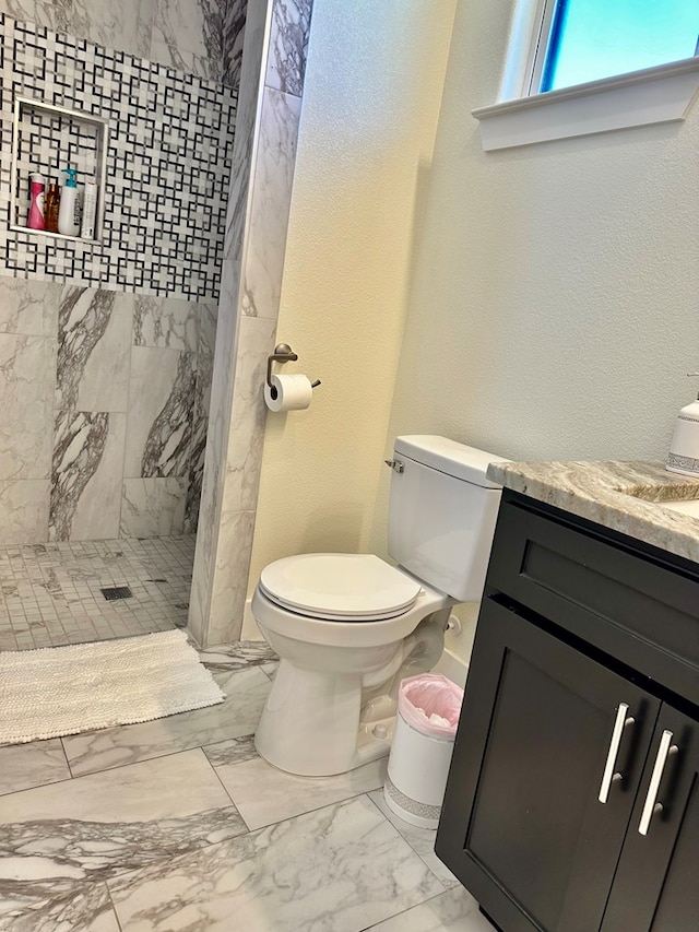 full bathroom with toilet, tiled shower, a textured wall, marble finish floor, and vanity