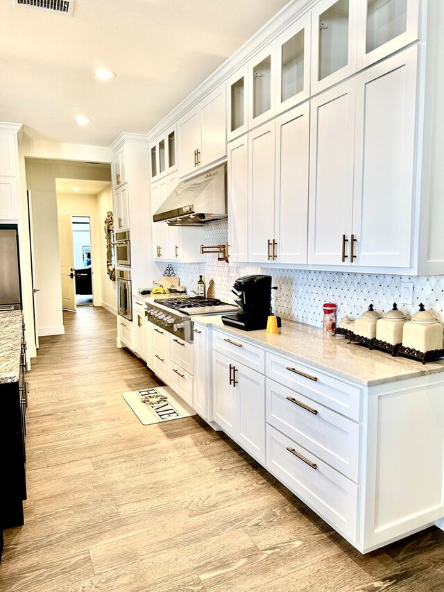 kitchen with under cabinet range hood, tasteful backsplash, white cabinetry, light wood-style floors, and appliances with stainless steel finishes