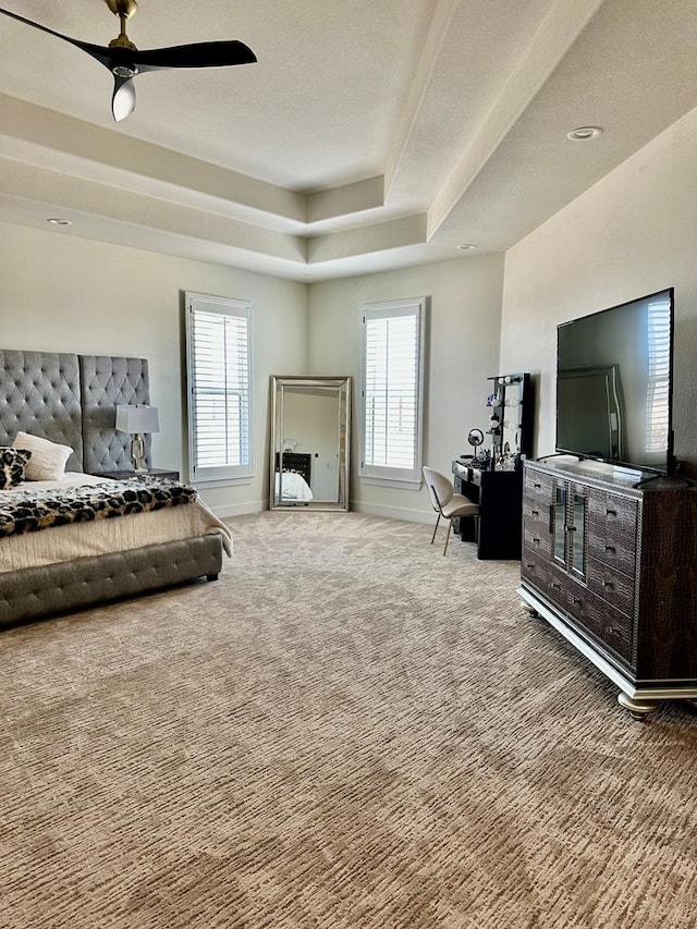 carpeted bedroom featuring a tray ceiling, multiple windows, baseboards, and ceiling fan