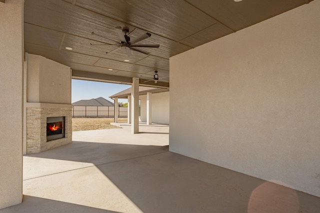 view of patio with a warm lit fireplace, a ceiling fan, and fence