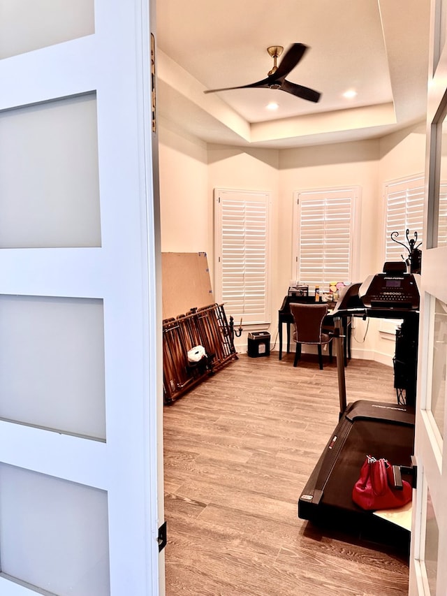 exercise area with a ceiling fan, a raised ceiling, recessed lighting, and wood finished floors