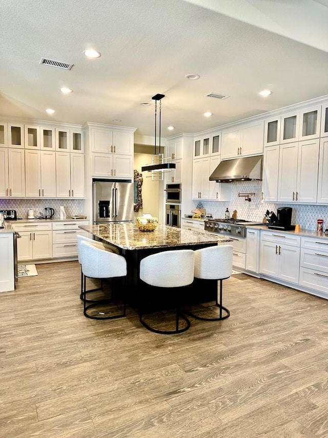 kitchen featuring a kitchen breakfast bar, visible vents, under cabinet range hood, and stainless steel appliances