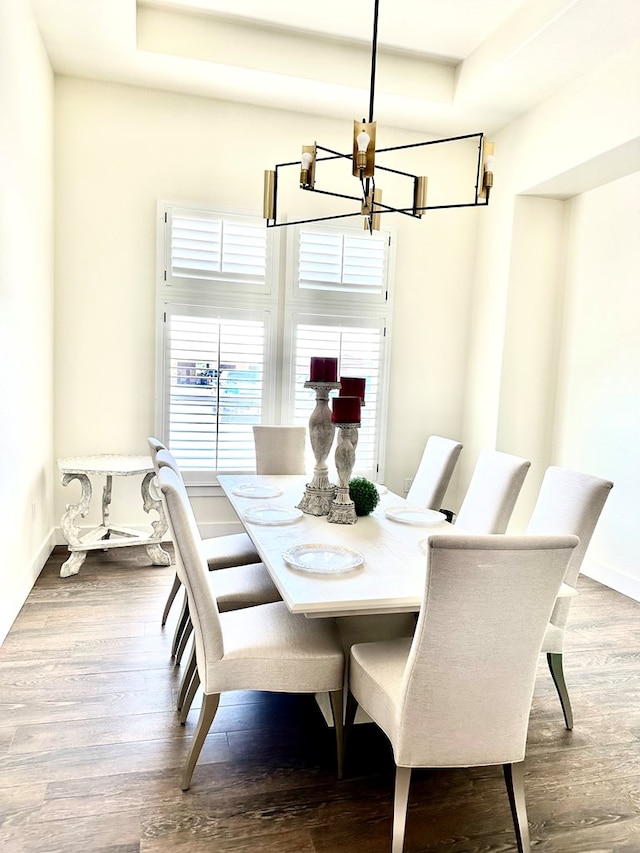 dining area with a notable chandelier, a raised ceiling, baseboards, and wood finished floors