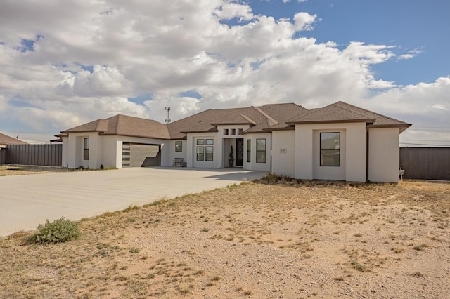 view of front of property with fence, a garage, driveway, and stucco siding