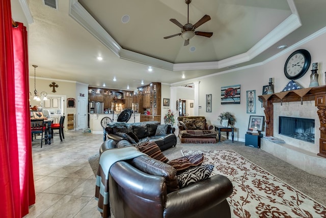 living room featuring a raised ceiling, ceiling fan, ornamental molding, a fireplace, and light tile patterned flooring