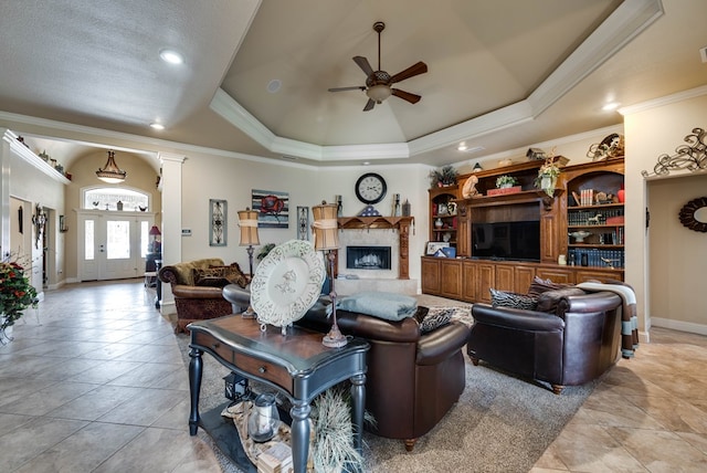 tiled living room featuring a tray ceiling, ceiling fan, ornamental molding, and decorative columns