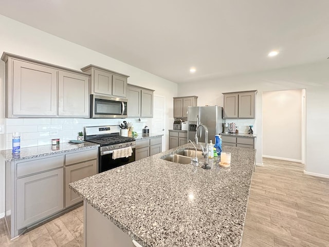 kitchen with sink, stainless steel appliances, tasteful backsplash, an island with sink, and light wood-type flooring