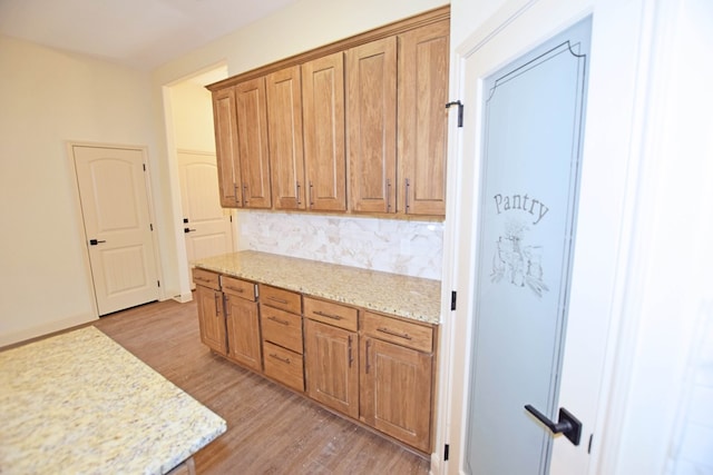 kitchen with light stone counters, light wood-type flooring, and backsplash