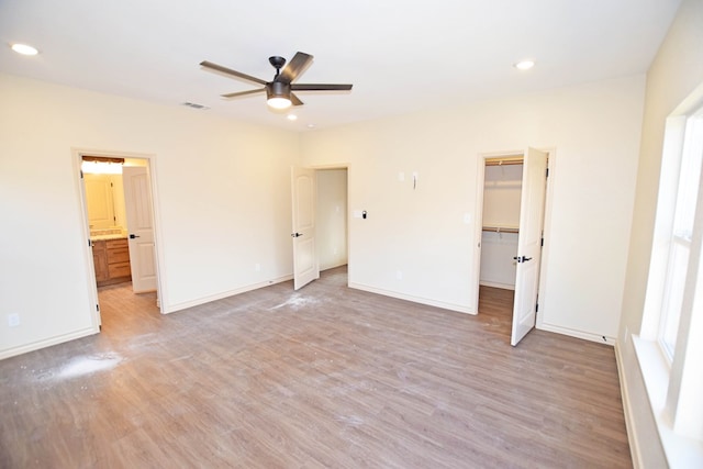 unfurnished bedroom with ceiling fan, light wood-type flooring, a walk in closet, and a closet