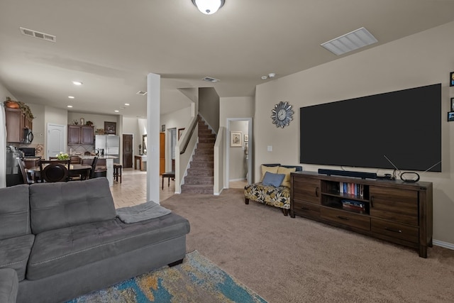 living room featuring stairs, visible vents, and light carpet