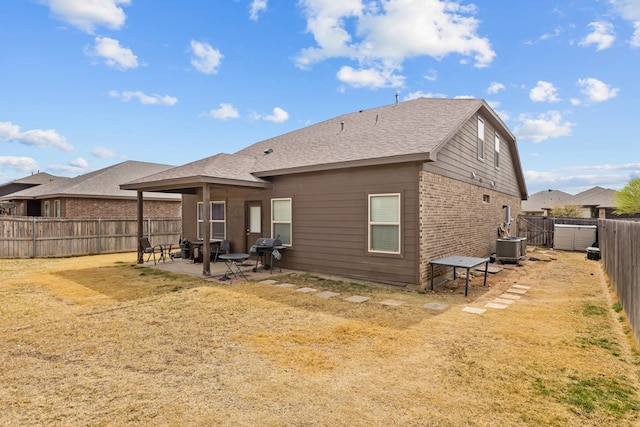 back of property with a yard, a fenced backyard, central air condition unit, a patio area, and brick siding