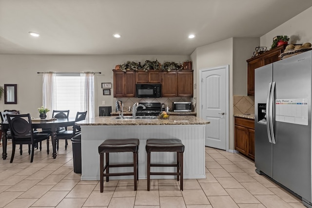 kitchen featuring a kitchen bar, a kitchen island with sink, a sink, light stone counters, and appliances with stainless steel finishes