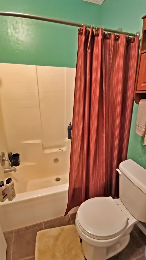 bathroom with tile patterned floors, shower / bath combination with curtain, and toilet