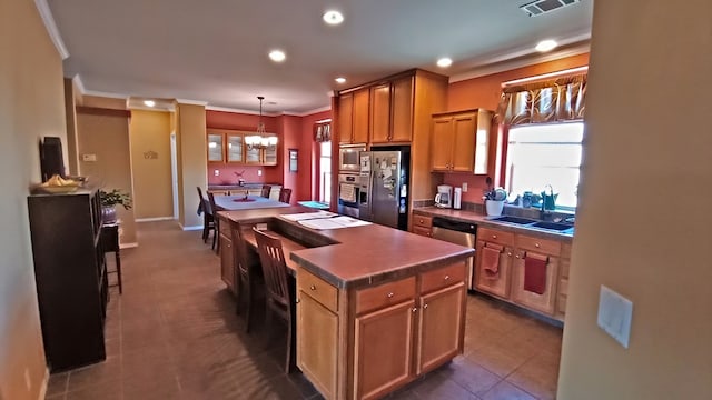 kitchen with ornamental molding, stainless steel appliances, sink, a center island, and hanging light fixtures