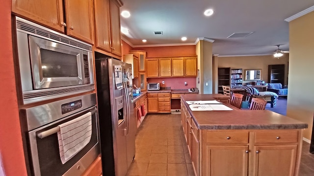 kitchen featuring light tile patterned flooring, ceiling fan, ornamental molding, a kitchen island, and stainless steel appliances